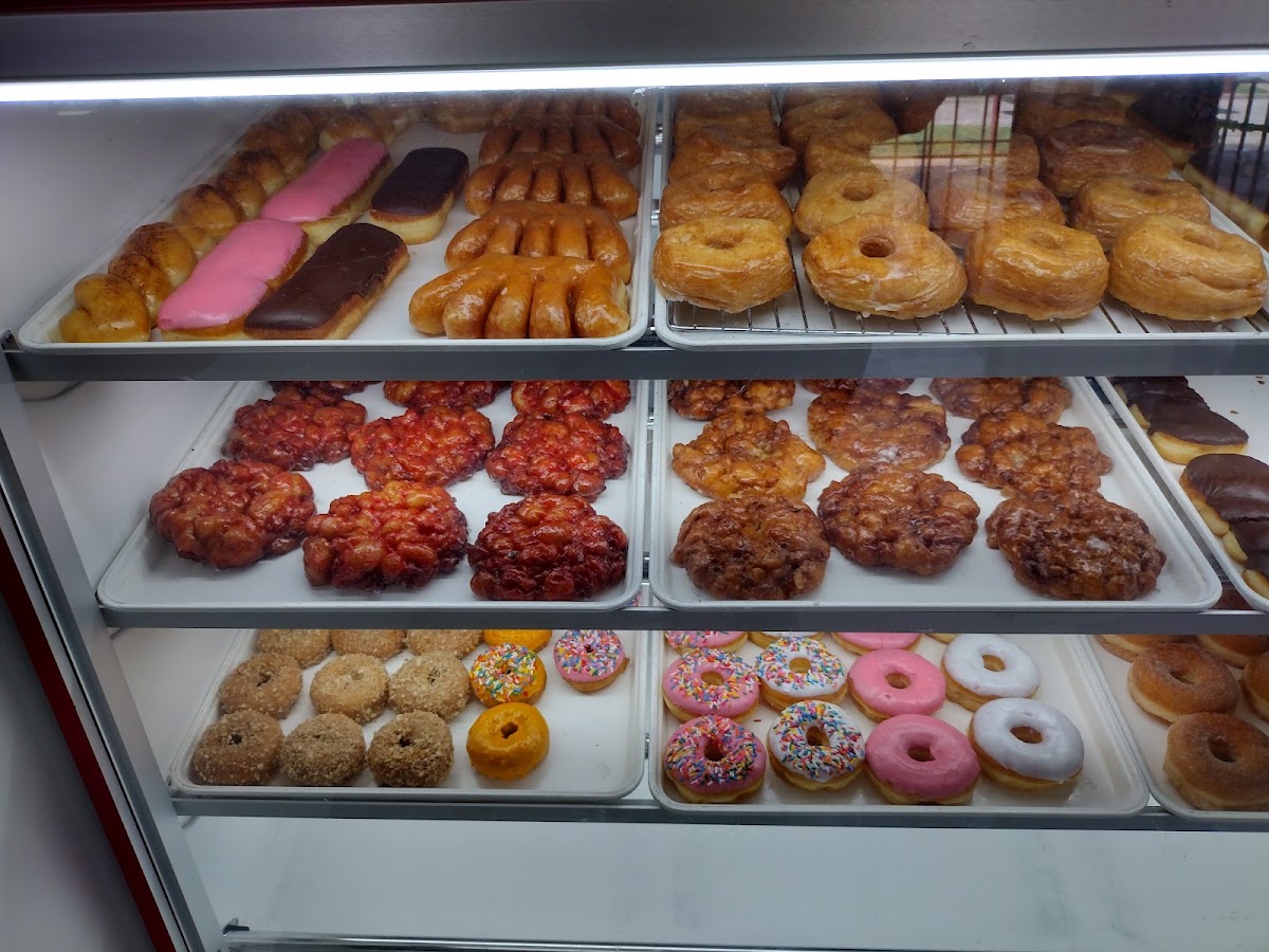 Trays of fresh donuts in the display case — apple fritters, glazed donuts, and iced donuts